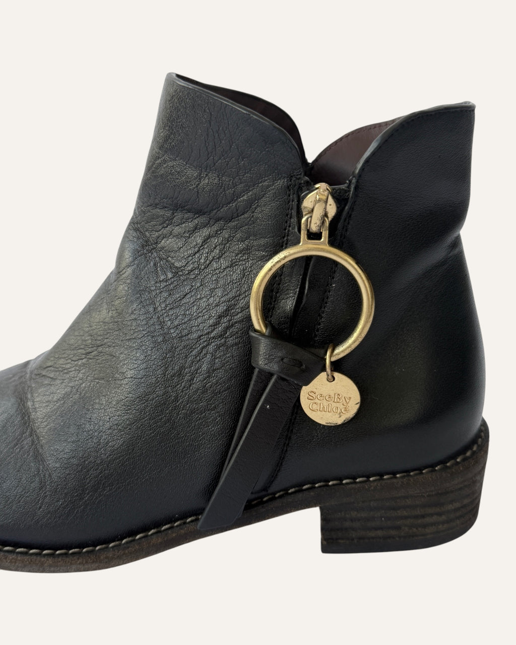 See by Chloé black leather moto ankle boot with gold ring zip pull, logo charm, and stacked heel