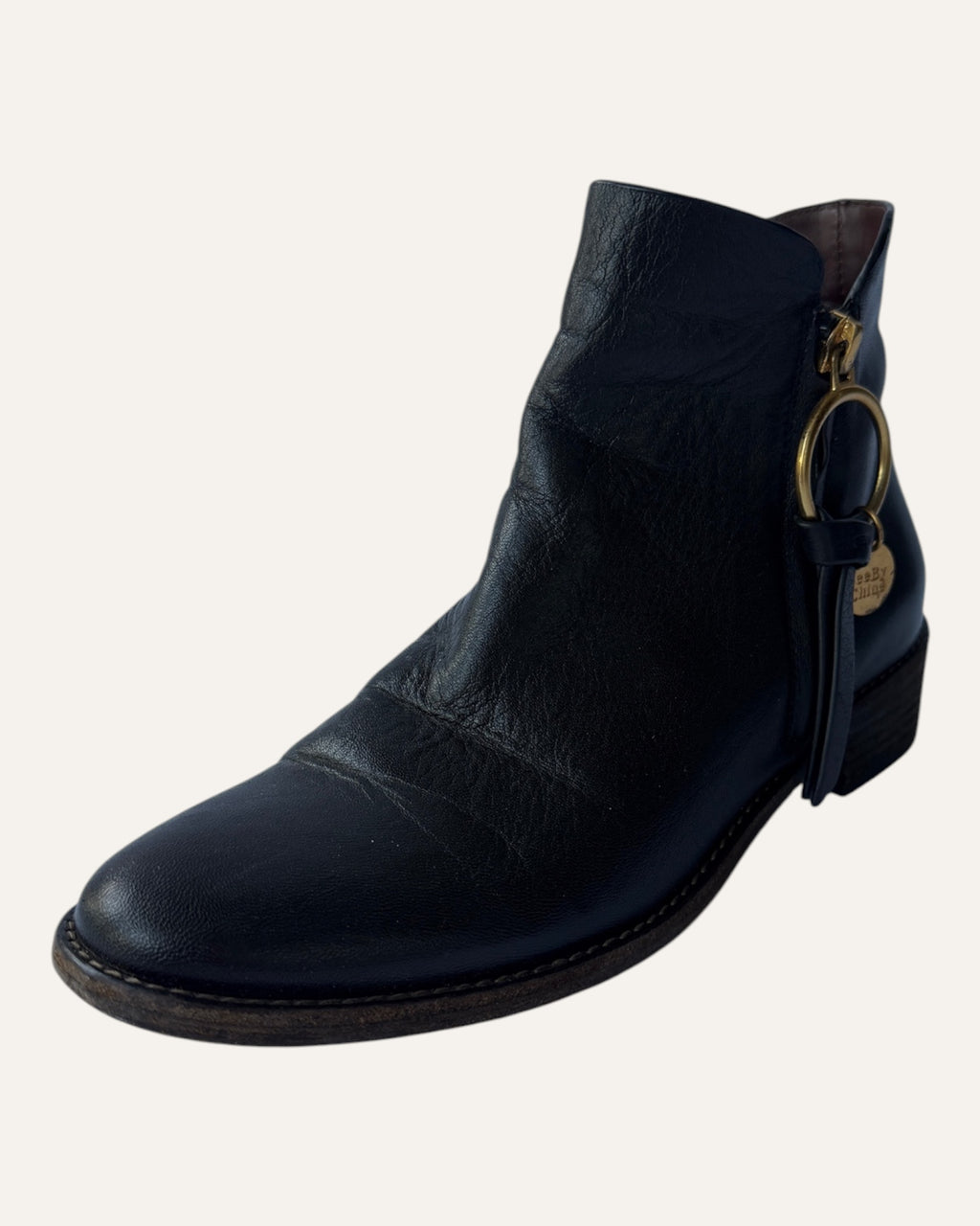 See by Chloé black leather moto ankle boot with gold ring zip pull, logo charm, and stacked heel