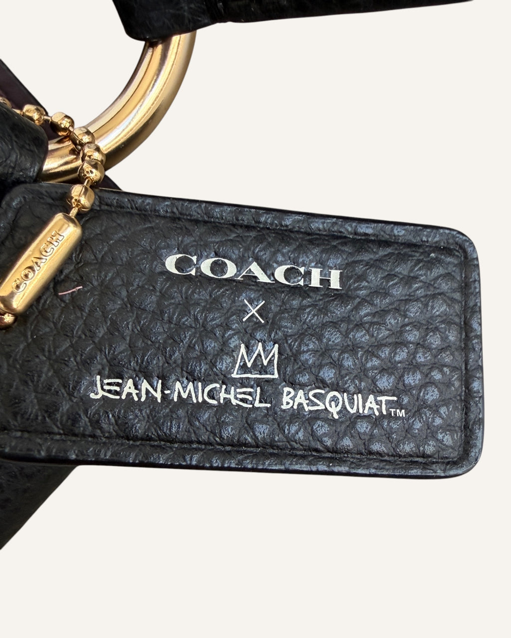 Close-up of a black pebbled leather Coach x Jean-Michel Basquiat bucket bag showing the crowned dinosaur artwork and gold-tone Coach New York logo plaque.