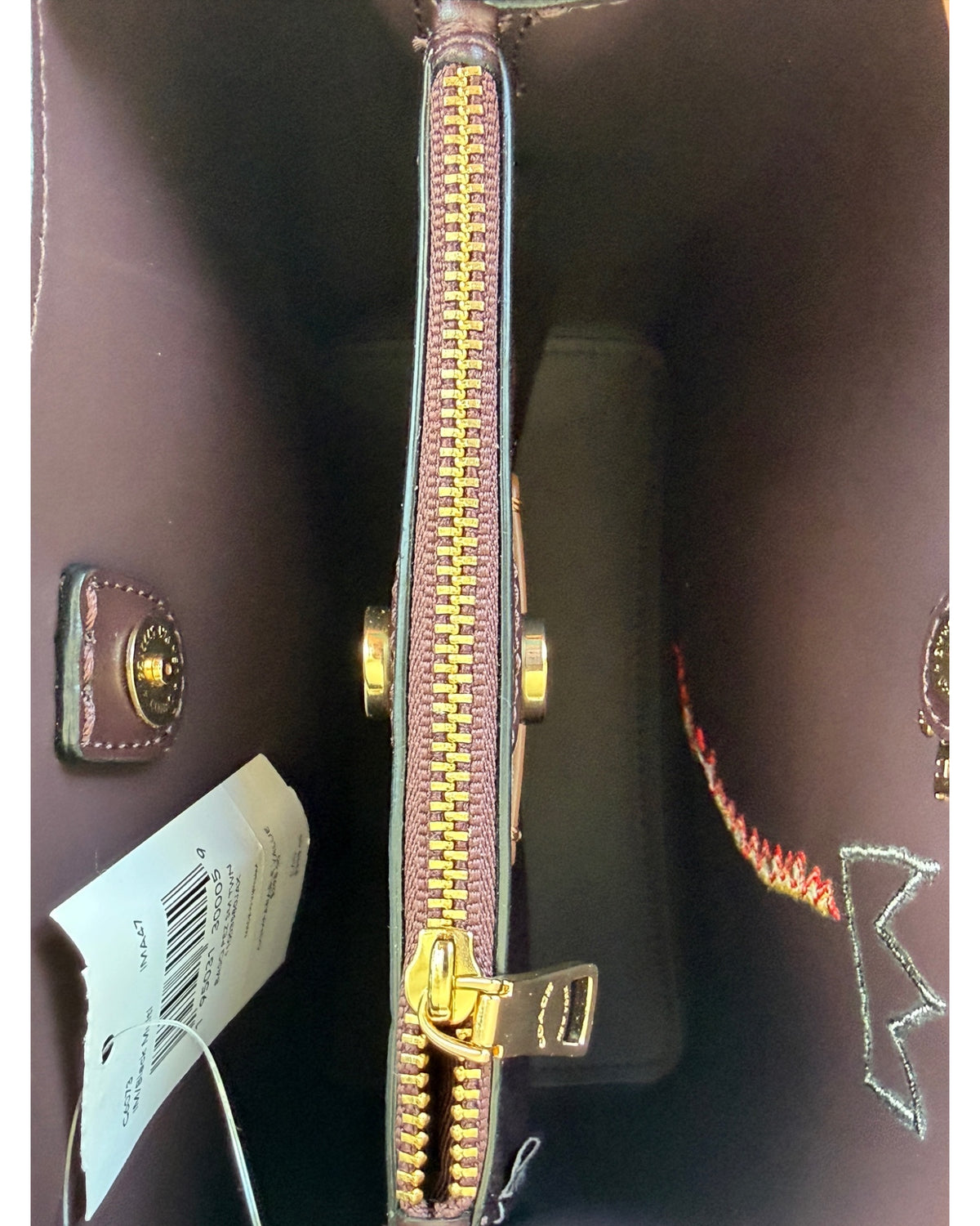 Close-up of a black pebbled leather Coach x Jean-Michel Basquiat bucket bag showing the crowned dinosaur artwork and gold-tone Coach New York logo plaque.